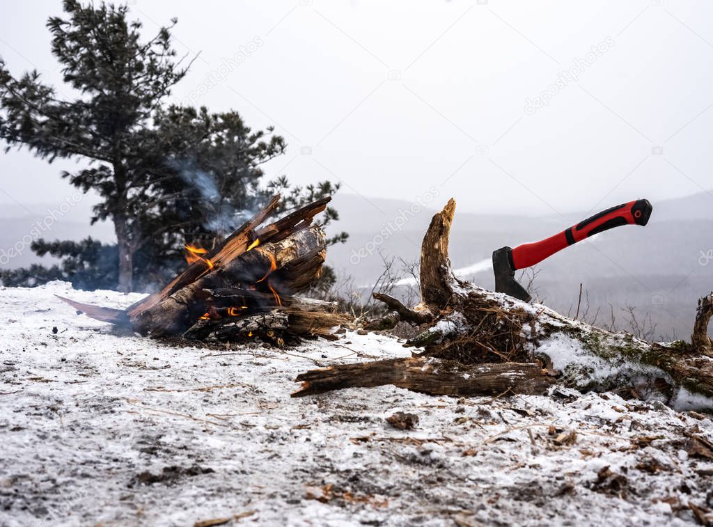 Camping: Ax with a red handle and a bonfire in the snowy mountains.