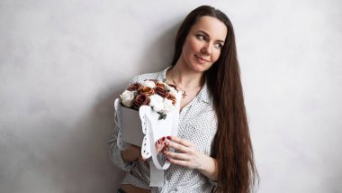 Güzel kıvırcık kız elinde gül ve şakayık çiçekleri olan bir kutu tutuyor ve aromalarının tadını çıkarıyor..