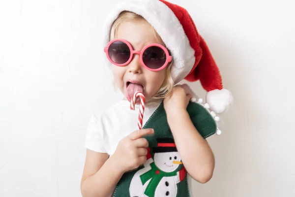 Boże Narodzenie: Mała dziewczynka w czerwonej czapce Mikołaja lizak w paski w jego rękach. — Zdjęcie stockowe