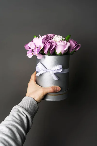 Flores en flor: Un ramo de rosas lila y blanca en una caja gris redonda en una mano masculina . — Foto de Stock