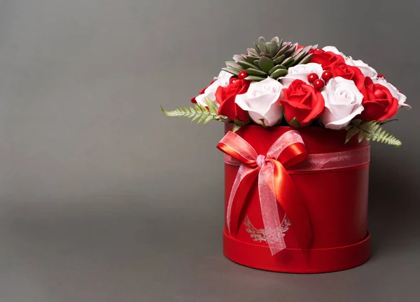 Flores en flor: Un ramo de rosas rojas y blancas en una caja redonda roja sobre un fondo gris . — Foto de Stock