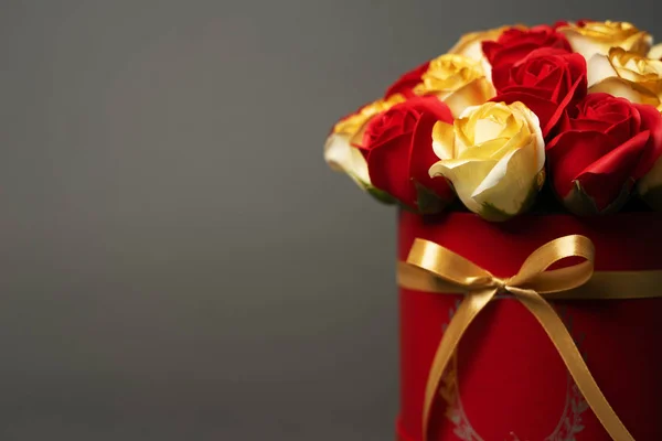 Flores en flor: Un ramo de rosas rojas y doradas en una caja redonda roja sobre un fondo gris . — Foto de Stock