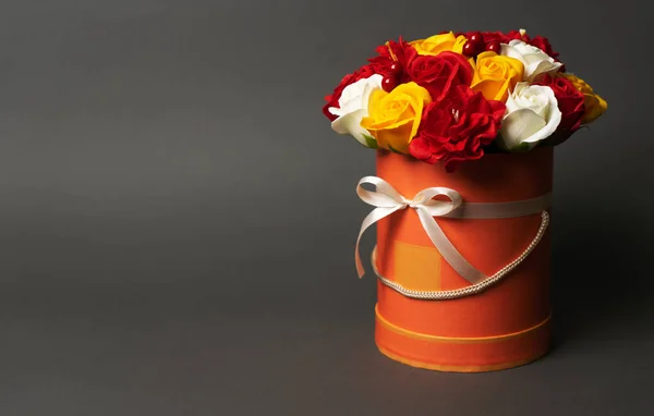 Flores en flor: Un ramo de rosas rojas y amarillas en una caja redonda sobre un fondo gris . — Foto de Stock