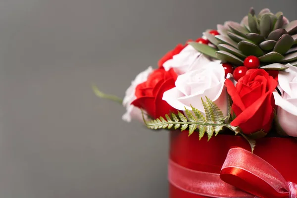 Flores en flor: Un ramo de rosas rojas y blancas en una caja redonda roja sobre un fondo gris . — Foto de Stock