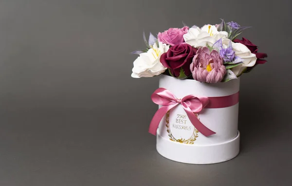 Flores en flor: cogollos rojos y rosados multicolores en una caja redonda blanca sobre un fondo gris . — Foto de Stock