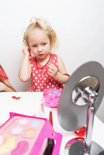 Παιδικά καλλυντικά: ένα μικρό κορίτσι επιδεικνύει στον καθρέφτη και χρησιμοποιεί μακιγιάζ. — Φωτογραφία Αρχείου