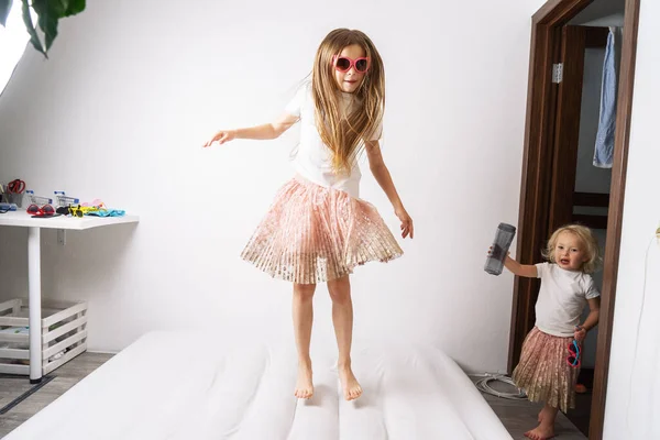 Κοριτσάκια με γυαλιά ηλίου και πανομοιότυπα φορέματα πηδάνε σε λευκό στρώμα. — Φωτογραφία Αρχείου
