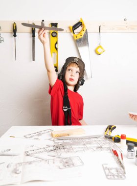 Çocukların hobileri: Pilot kaskı takan küçük bir çocuk, plastik parçalardan büyük ölçekli bir uçak modeli üretiyor..