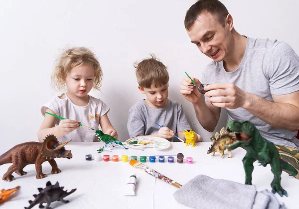 Hobby: pai com filho e filha pintar pequenas figuras de dinossauros com tinta e uma escova. — Fotografia de Stock