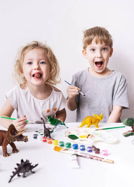 Crianças menino e menina rir alegremente jogar e pintar com figuras de brinquedo e escova de dinossauros de brinquedo . — Fotografia de Stock