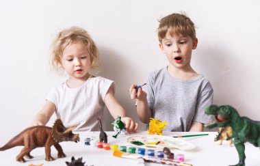 Children a boy and a girl are passionate and paint with figures and brush figures of toy dinosaurs.