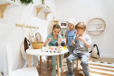 Easter holiday: children sit at the table and paint eggs with paints and brushes. Family portrait.