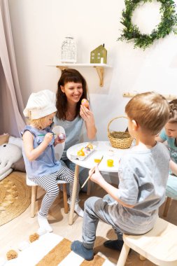 Easter holiday: mother and children sit at the table and paint eggs with paints. Family portrait.