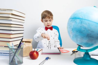 Okula dönersek, bir çocuk masanın başına oturur ve pusula kullanarak bir not defteri çizer. Portre.