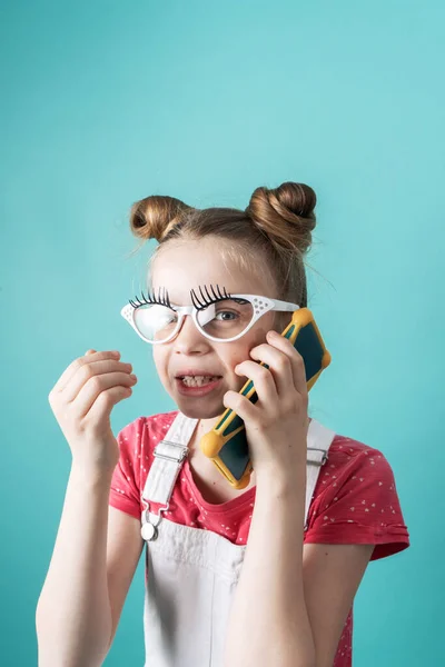 Beauty industry: A girl with glasses and false eyelashes makes a phone call and gossips. Comic studio portrait.