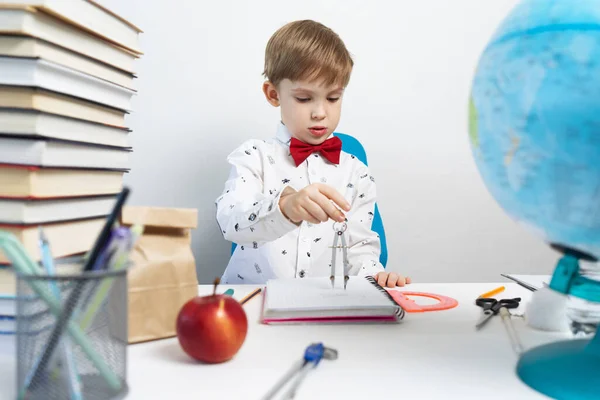 Назад до школи: Хлопчик сидить за столом і малює в блокноті за допомогою циркуля . — стокове фото