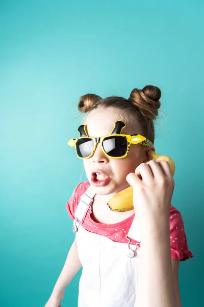 Moderne technologie: Een tienermeisje met een grappige bril gebruikt een gele banaan als telefoon. — Stockfoto