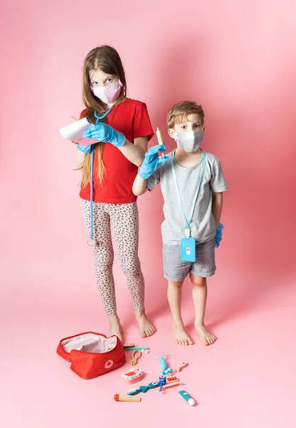 Persoonlijke beschermingsmiddelen: kinderen een jongen en een meisje met medische maskers en blauwe handschoenen spelen met een kinderset van een arts. — Stockfoto