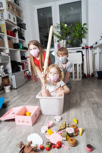 Fique em casa: crianças em máscaras médicas brincam com brinquedos e andam em uma caixa branca . — Fotografia de Stock