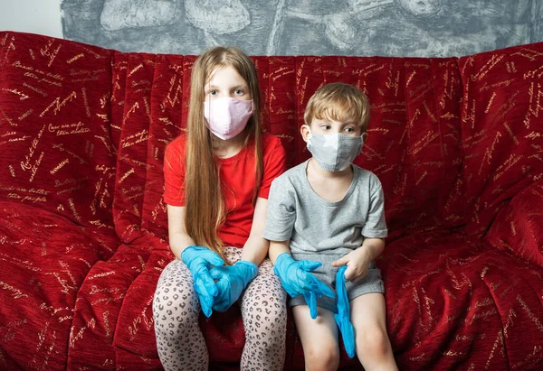 Stay at home: a boy and a girl in a medical mask and gloves are sitting at home on the couch.