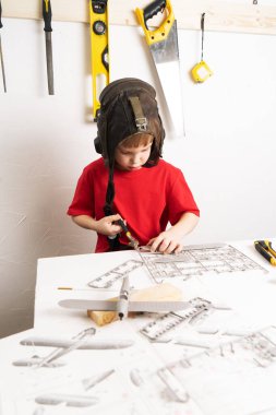 Çocukların hobileri: Pilot kaskı takmış küçük bir çocuk bir devre kullanarak plastik parçalardan uçağın büyük ölçekli bir modelini yapıyor. Portre.