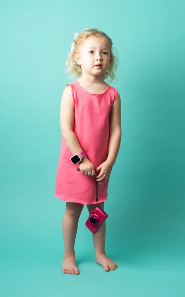 Niña en un vestido rosa con una pequeña cámara rosa sobre un fondo verde . — Foto de Stock