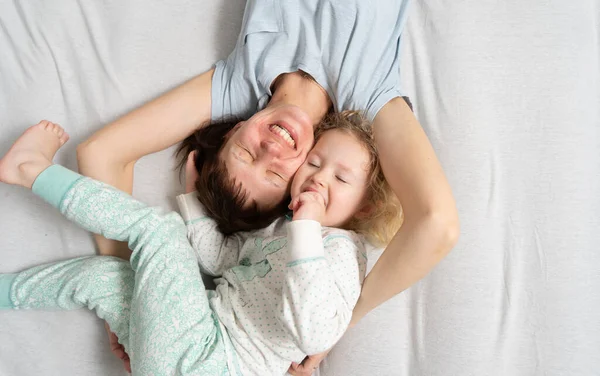 家族の時間:お母さんと娘はベッドの上で抱き合って笑って嘘をついている. — ストック写真