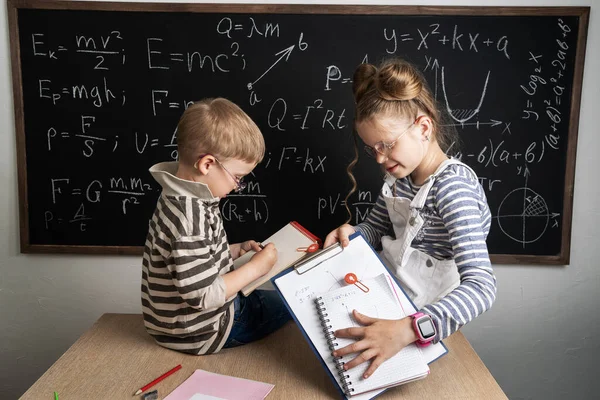 Back to school: a boy and a girl in glasses sit at a desk and make notes in a notebook. Portrait.