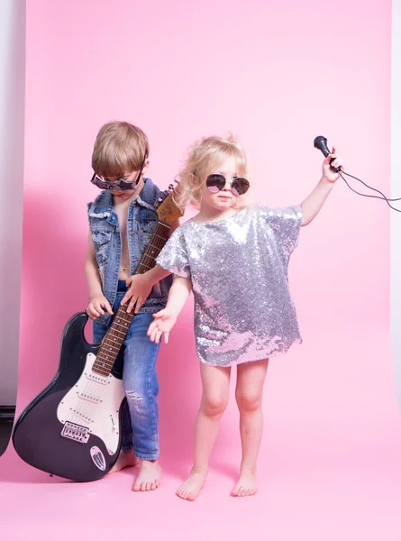 Cultura Pop: Niños un niño con una guitarra y una niña con un micrófono pretenden ser músicos populares y realizan un concierto en casa . — Foto de Stock