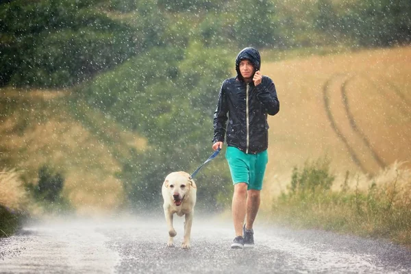 Hombre con perro bajo fuerte lluvia — Foto de Stock