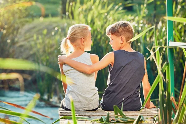 Двое детей сидят на пирсе озера — стоковое фото