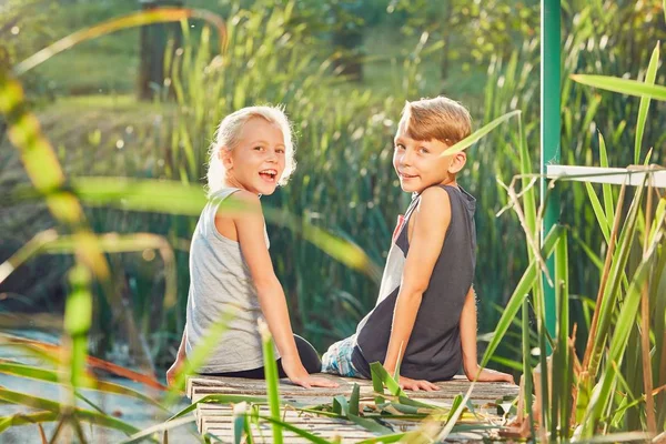 Two children sitting on the pier of the lake — Stock Photo, Image