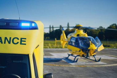 Ambulance car against helicopter of emergency medical service. Selective focus on blue flasher. clipart