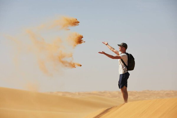 Happy traveler in desert. Young man throwing sand in wind. Abu Dhabi, United Arab Emirates