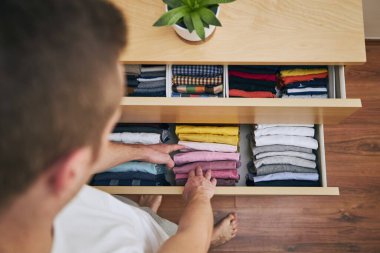 Organizing and cleaning home. Man preparing orderly folded t-shirts in drawer.  clipart