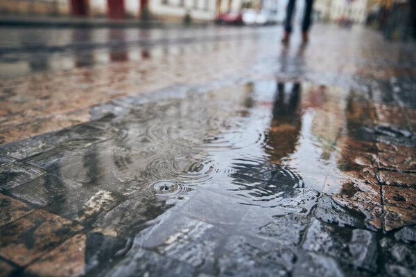 Rain in city. Close-up view of puddle on city street and reflection of man with umbrella. Gloomy day in Prague, Czech Republic.