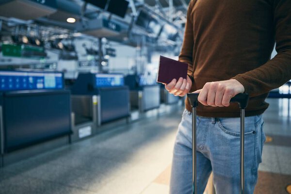 Passenger against check-in counter at airport. Hands of young man holding suitcase and passport. 