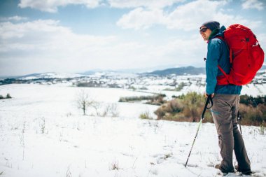Sırt çantalı ve sırıklı bir turist. Bahar karlı dağlarda güneşli bahar şafağı. Yürüyüş, kamp malzemeleri..