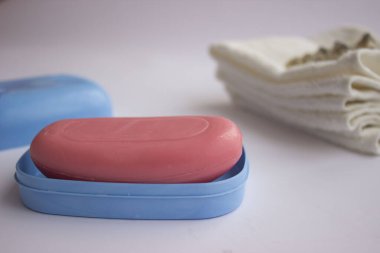Mavi sabunlukta pembe el sabunu. Havlular onun yanında yatıyor. İç tarafında bir demet lavanta ve deniz kabuğu var. Mavi bir sabun kabı. Havlular onun yanında yatıyor. İç tarafında bir demet lavanta ve deniz kabuğu var..
