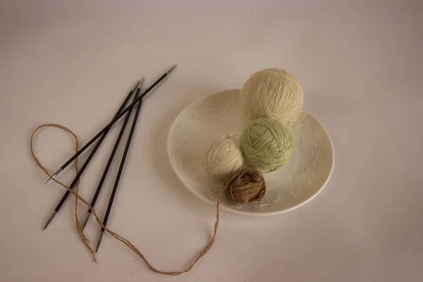 White Cup with wool balls. The black needles are next to the saucer. The balls are on the saucer. Tropical colors. Natural materials for needlework. handmade in miniature. Knitting.