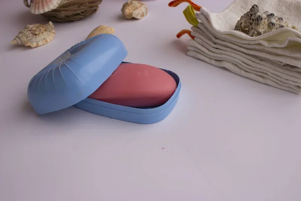 Mavi sabunlukta pembe el sabunu. Havlular onun yanında yatıyor. İç tarafında bir demet lavanta ve deniz kabuğu var. Mavi bir sabun kabı. Havlular onun yanında yatıyor. İç tarafında bir demet lavanta ve deniz kabuğu var..