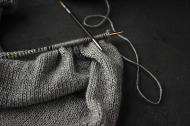 Gümüş iplik iğnelerinin üzerinde örgü örmek karanlık bir arka planda yatar..