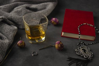 Karanlık bir arka planda berrak bir bardak viski duruyor. Yanında kırmızı bir kitap var..