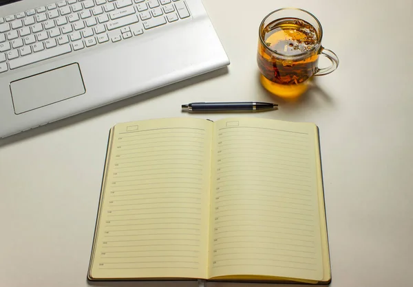 A glass of herbal soothing tea sits on a white table next to a notebook and pen. The concept of working at home.