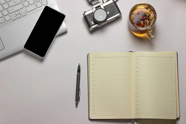 Bir bardak bitkisel yatıştırıcı çay beyaz bir masanın üzerinde bir defter ve kalemin yanında duruyor. Evde çalışma kavramı..