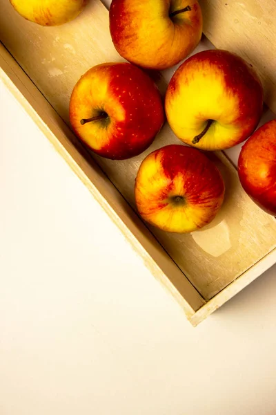 The apples are in a white wooden box on a white background. Red and yellow ripe apples.