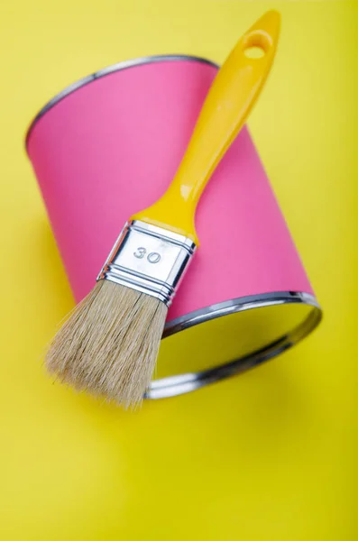 Can of pink paint and paintbrush on yellow background — Stock Photo, Image