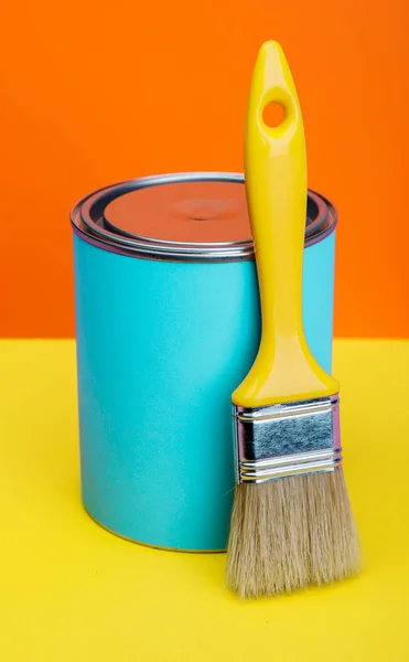 Can of blue paint and paintbrush on orange and yellow background — Stock Photo, Image