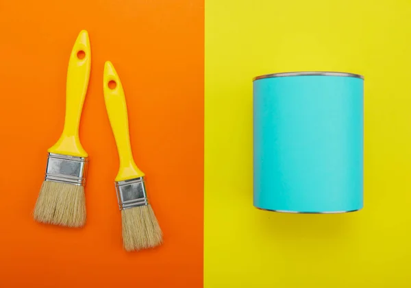 Can of blue paint and paintbrush on orange and yellow background — Stock Photo, Image