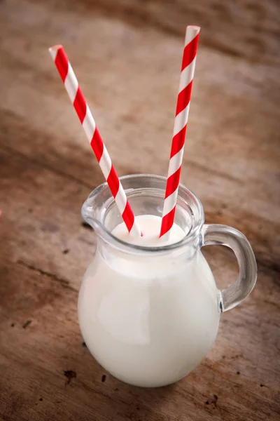 Tarro de leche con grandes pajitas a rayas de papel rojo sobre fondo de madera — Foto de Stock